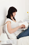 Gorgeous brunette woman relaxing with her laptop while sitting o