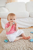 Smiling baby playing with puzzle pieces while sitting on a carpe
