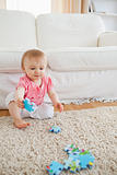 Lovely blond baby playing with puzzle pieces while sitting on a 