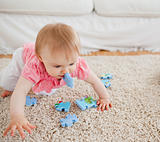 Lovely blond baby playing with puzzle pieces on a carpet