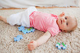 Cute blond baby playing with puzzle pieces while lying on a carp