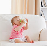 Lovely blond baby bottle-feeding while sitting on a sofa