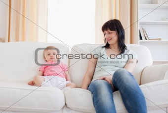 Pretty woman looking at her baby while sitting on a sofa