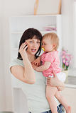 Lovely woman on the phone while holding her baby in her arms