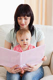 Attractive woman holding her baby and a book in her arms while s