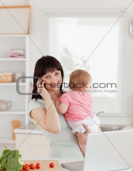 Beautiful brunette woman on the phone while holding her baby in 