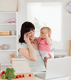 Attractive brunette woman on the phone while holding her baby in