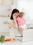 Pretty brunette woman on the phone while holding her baby in her