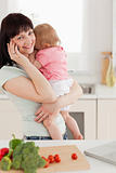 Cute brunette woman on the phone while holding her baby in her a