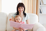 Good looking woman holding her baby and a book in her arms while