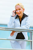 Smiling business woman leaning on railing at office building and talking on mobile
