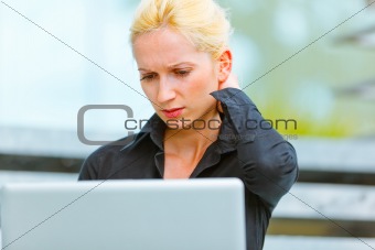 Concentrated business woman sitting on stairs at office building and using laptop
