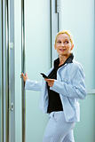 Smiling business woman entering office building holding mobile in hand
