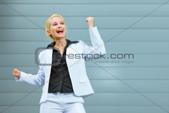 Pleased business woman standing at office building  and rejoicing her success 
