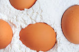fresh organic brown eggs on white flour powder
