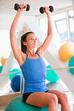 Woman Using Hand Weights On Swiss Ball At Gym