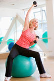 Woman Using Hand Weights On Swiss Ball At Gym