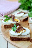 snacks sandwiches with egg and anchovies on a wooden board