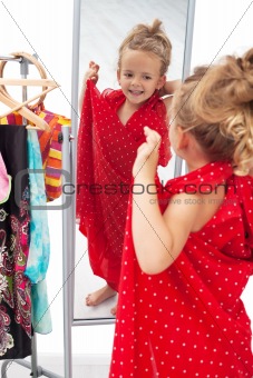 Happy little girl trying on dresses in front of mirror