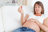 Attractive pregnant woman holding a cigarette while lying on a sofa