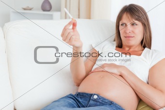 Attractive pregnant woman holding a cigarette while lying on a sofa
