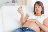 Beautiful pregnant woman holding a cigarette while lying on a sofa
