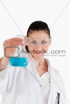 Dark-haired scientist with safety glasses holding a blue flask