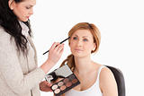 Cute blond-haired woman having her make up done by a make up art