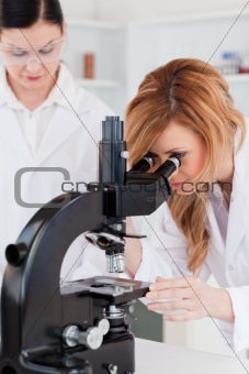 Young scientist looking through a microscope with her assistant