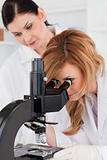Cute scientist looking through a microscope with her assistant