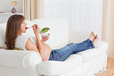 Pretty pregnant woman eating a salad while lying on a sofa