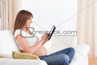 Lovely pregnant woman relaxing with a computer tablet while sitt