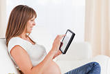Beautiful pregnant woman relaxing with a computer tablet while s