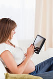 Good looking pregnant woman relaxing with a computer tablet whil