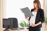 Beautiful pregnant female holding a file while standing