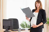 Attractive pregnant female holding a file while standing