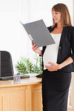 Charming pregnant female holding a file while standing