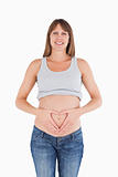 Lovely pregnant female posing while forming a heart with her hands