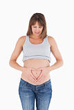 Attractive pregnant female posing while forming a heart with her