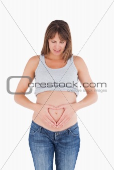 Attractive pregnant female posing while forming a heart with her