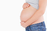 Side view of a young pregnant woman caressing her belly while st