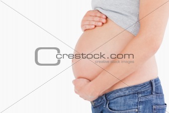 Side view of a young pregnant woman caressing her belly while st