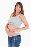 Beautiful pregnant woman measuring her belly while standing