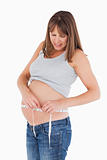 Attractive pregnant woman measuring her belly while standing
