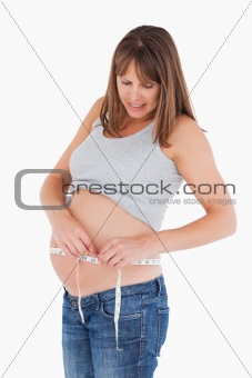 Attractive pregnant woman measuring her belly while standing