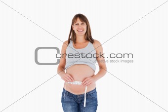 Charming pregnant woman measuring her belly while standing