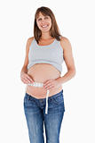 Cute pregnant woman measuring her belly while standing