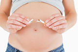 Young pregnant woman holding a broken cigarette while standing