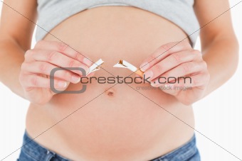 Young pregnant woman holding a broken cigarette while standing