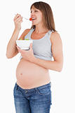 Beautiful pregnant woman eating a cherry tomato while holding a 